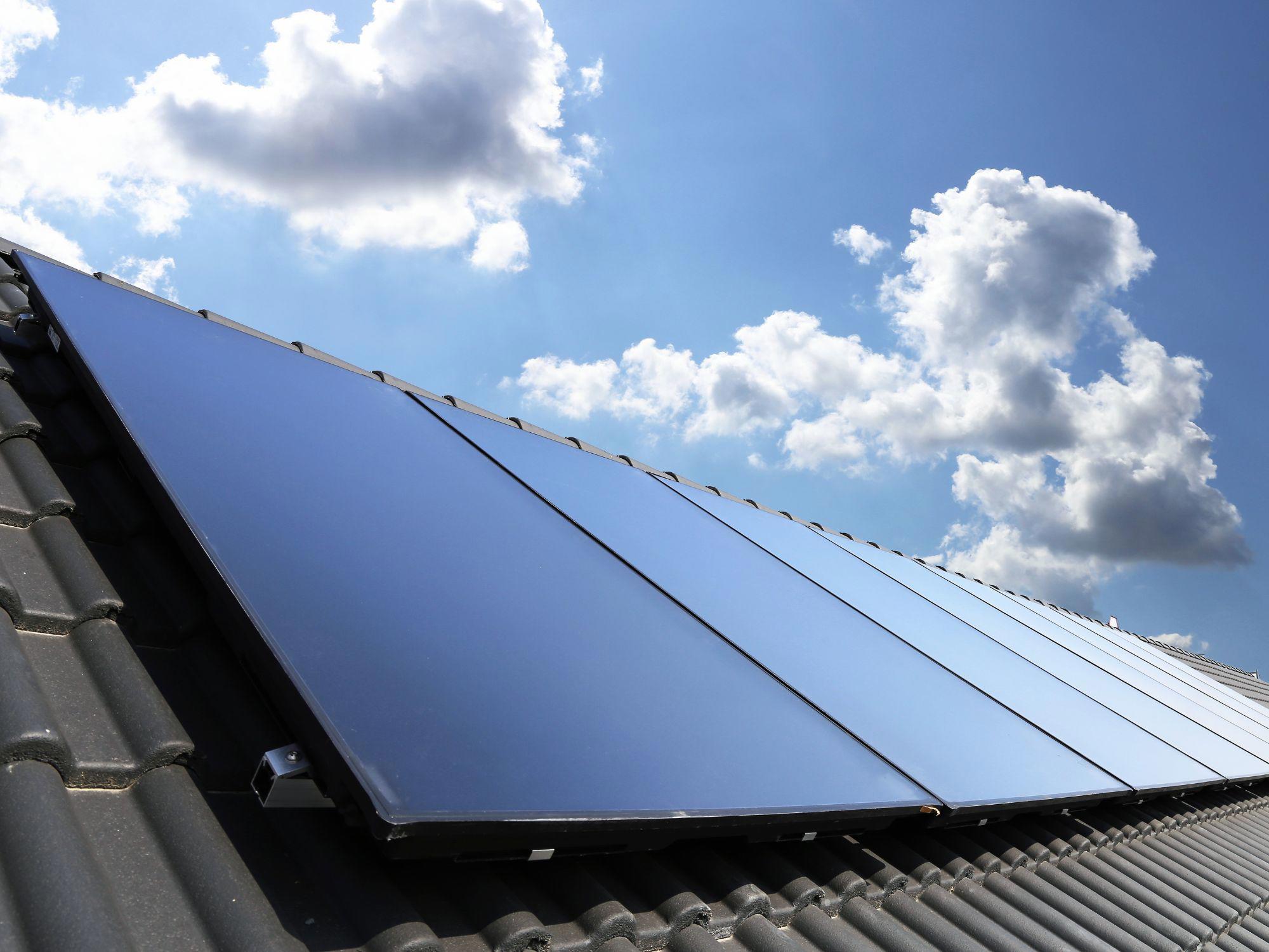 Solar panels installed on a tiled rooftop under a partly cloudy sky, reflecting sunlight.